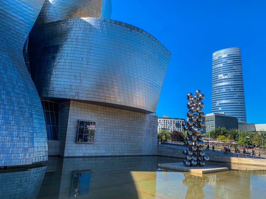 Modern architecture of Guggenheim Museum Bilbao and reflective sculpture under clear sky.